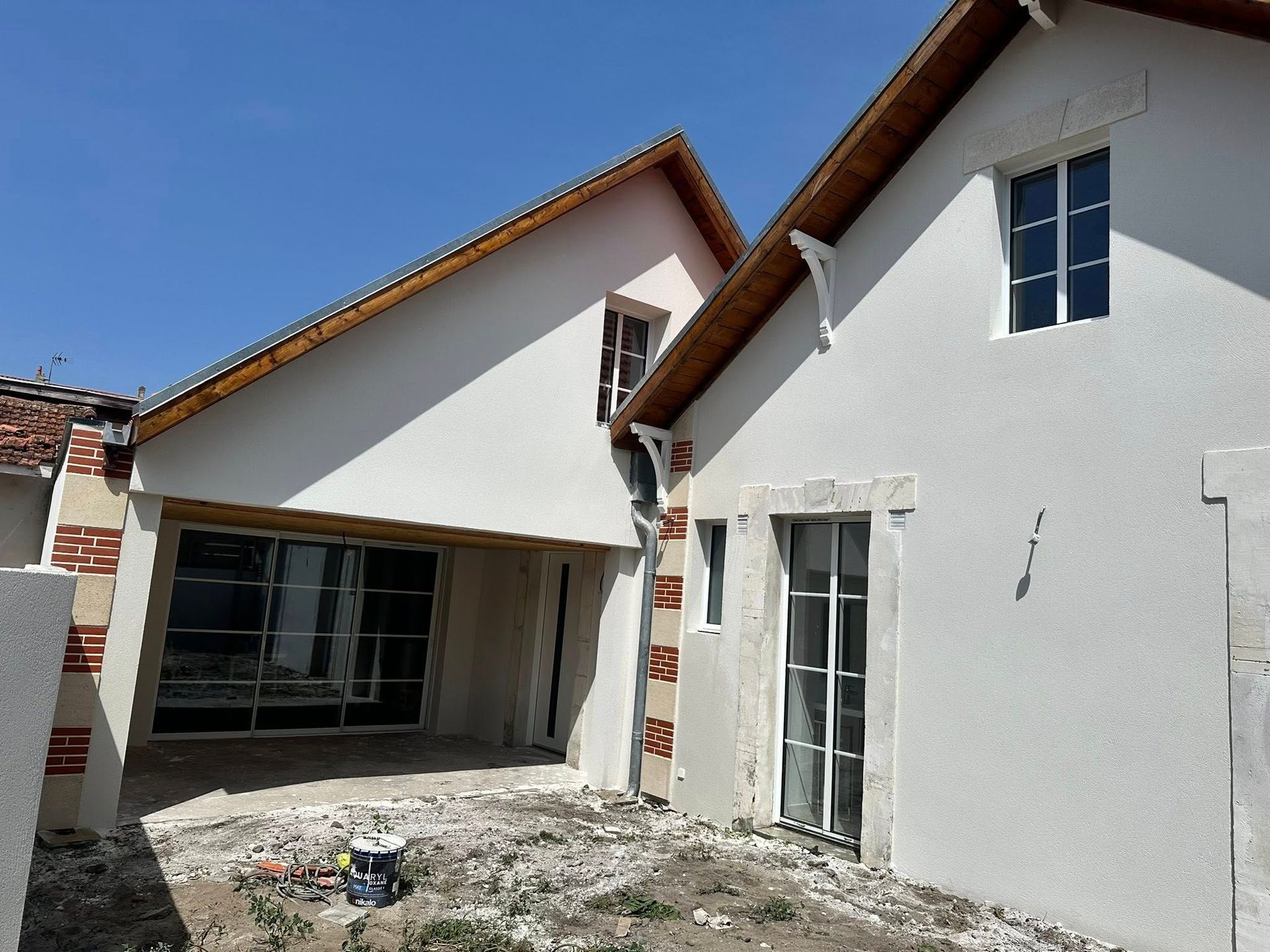 Une maison blanche à deux étages avec un toit en bois, des éléments en pierre claire
