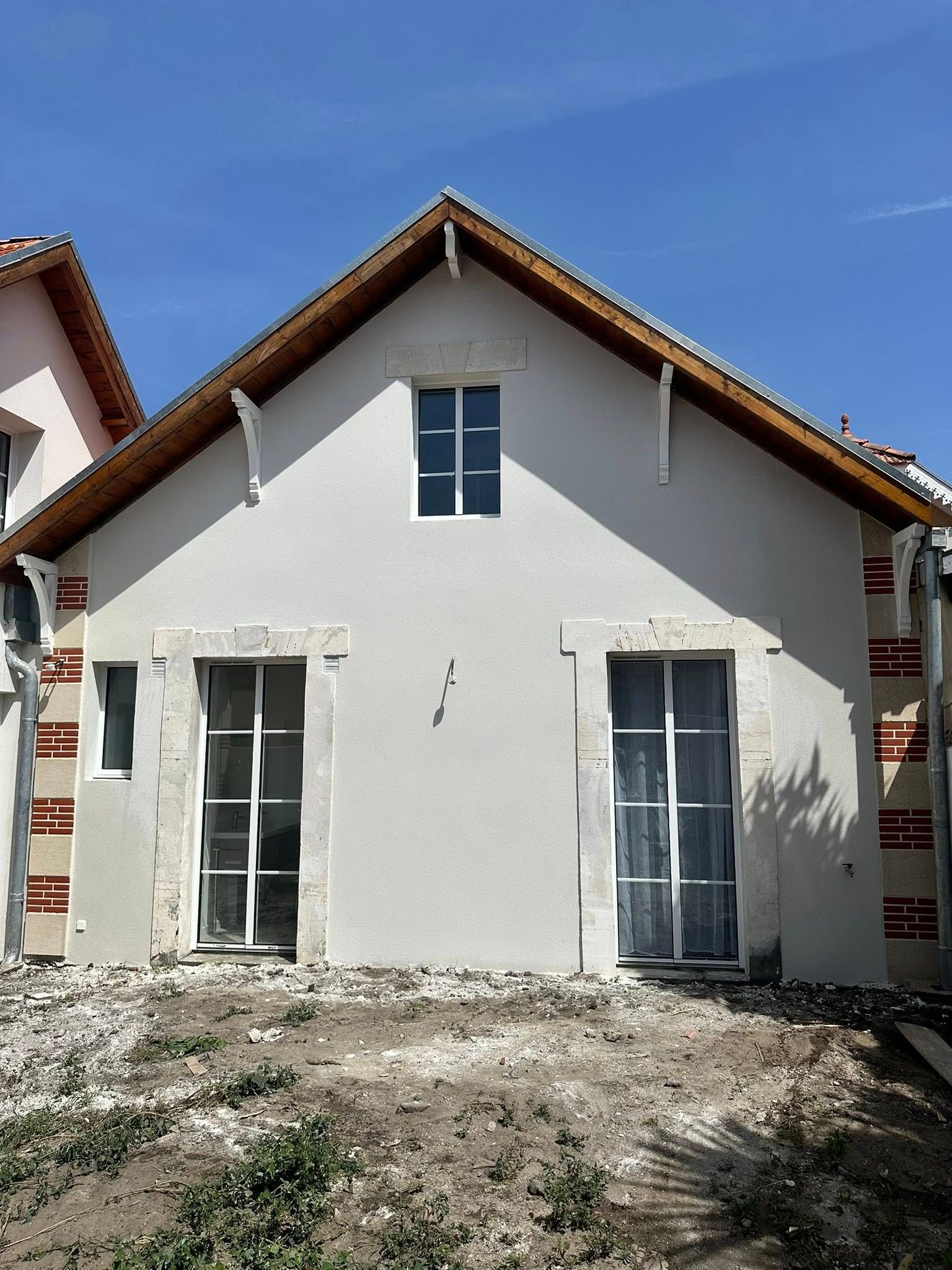 Façade de maison à pignon de couleur claire avec une fenêtre centrale.