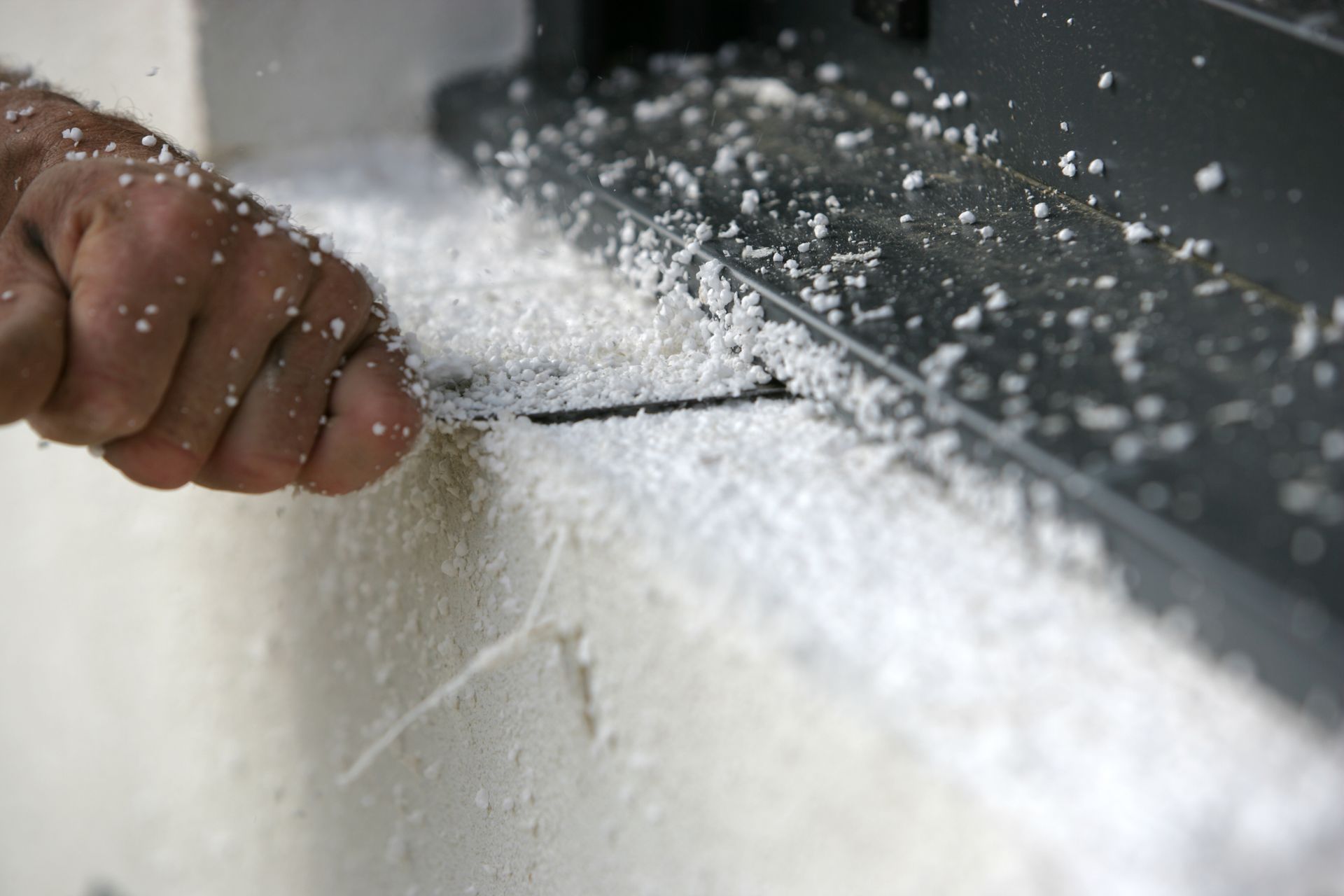 Une main utilise un outil pour gratter les débris de mousse isolante du bord d'un cadre de fenêtre.