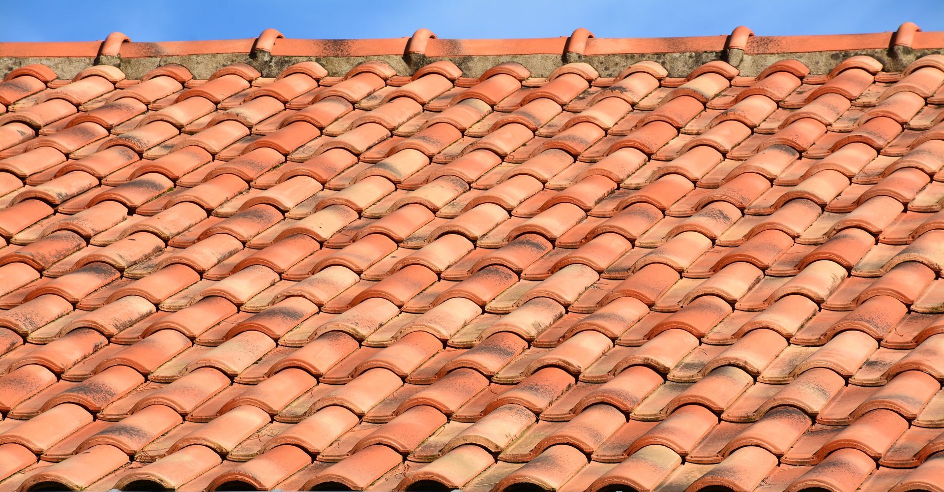 Un motif de tuiles de terre cuite se chevauchant sous un ciel bleu clair.
