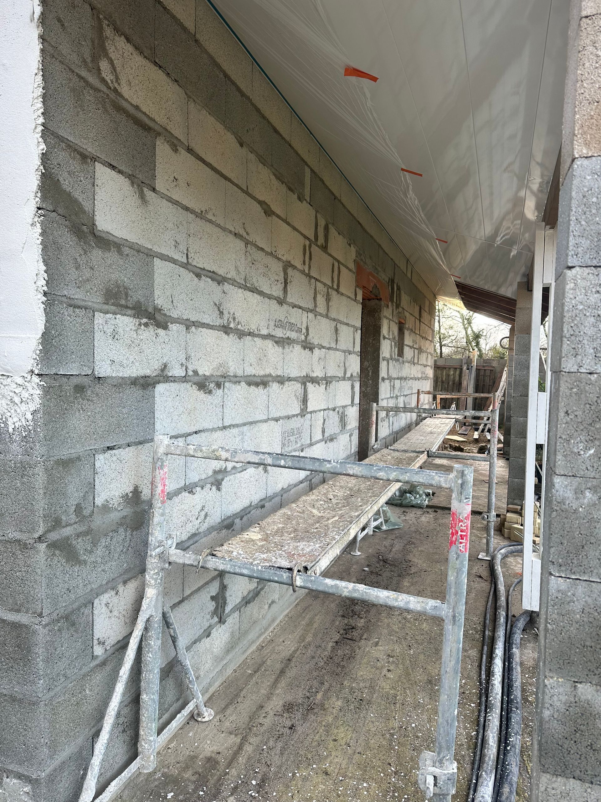 Mur en parpaings gris en construction, avec un échafaudage métallique au premier plan.