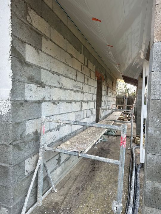 Mur en parpaings gris en construction, avec un échafaudage métallique au premier plan.