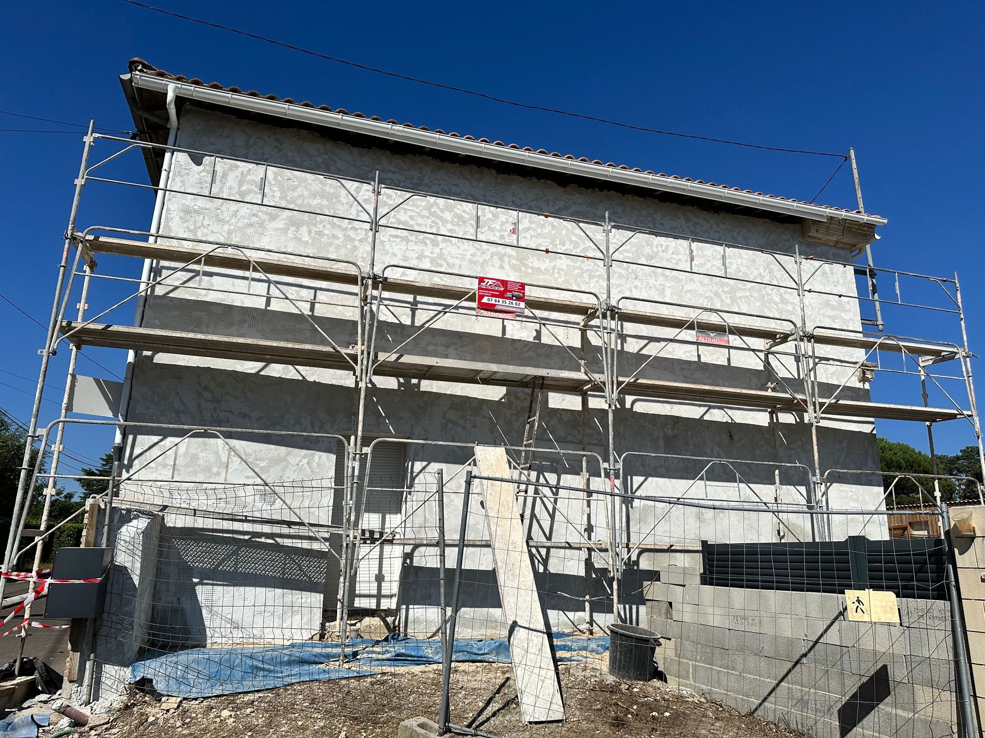 Un bâtiment clair en construction, recouvert d'échafaudages métalliques, se détache sur un ciel bleu clair.