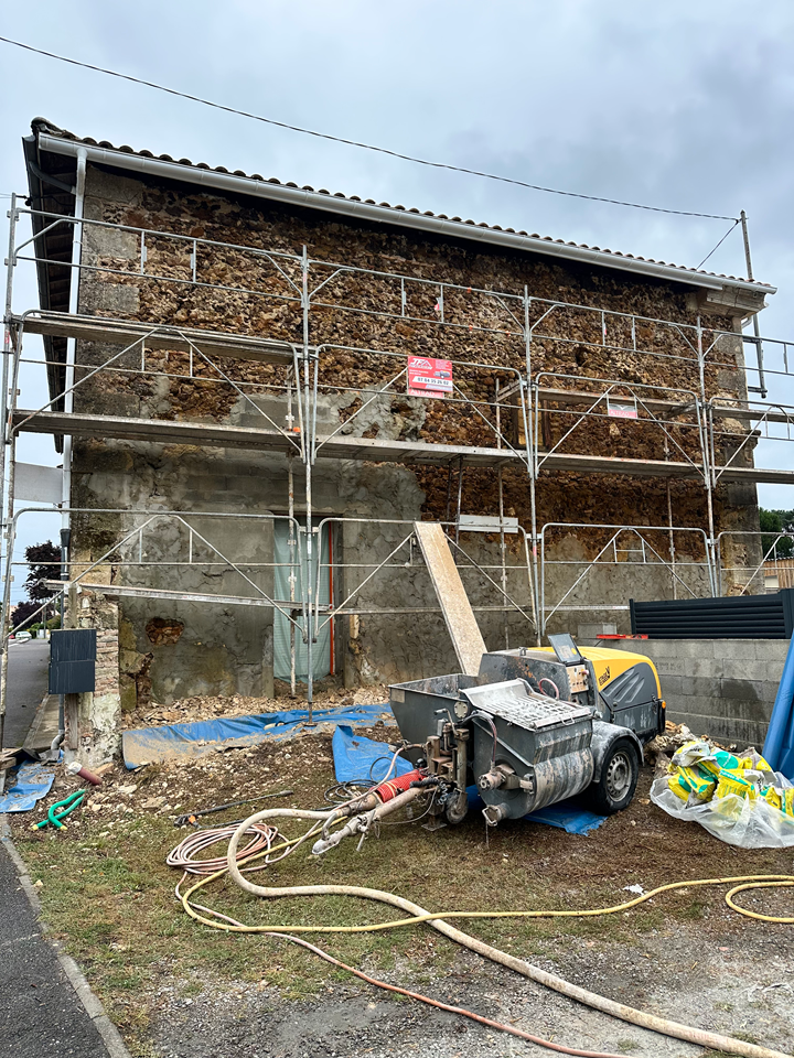 Des échafaudages entourent un vieux bâtiment en pierre dont la façade extérieure est en cours de réparation.