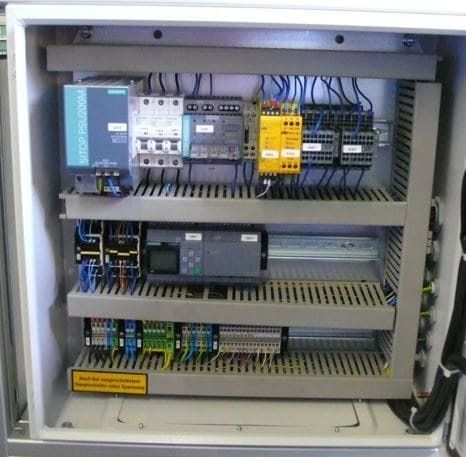 Offener elektrischer Schaltschrank mit Verkabelung, Relais, Leistungsschaltern und Industriemodulen.