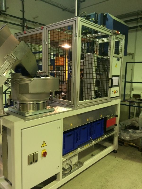 Industriemaschine mit Metallförderband und Sicherheitskäfig in einer Fabrikhalle.