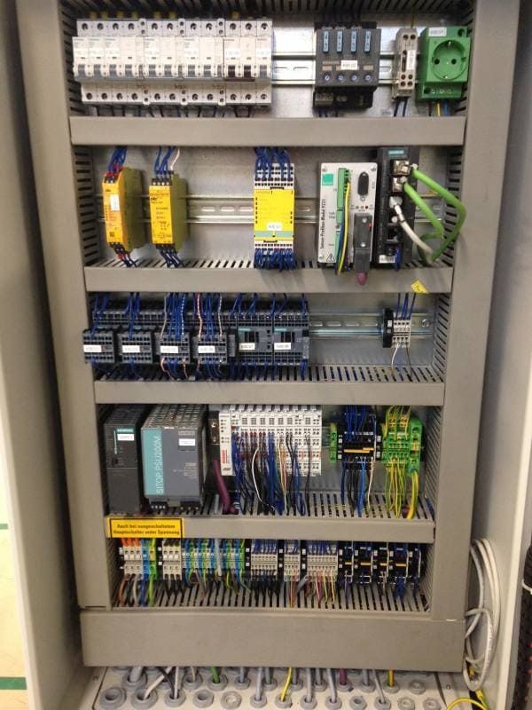 Elektrischer Schaltschrank mit Leistungsschaltern, Relais, Verkabelung und grünen Klemmenblöcken.