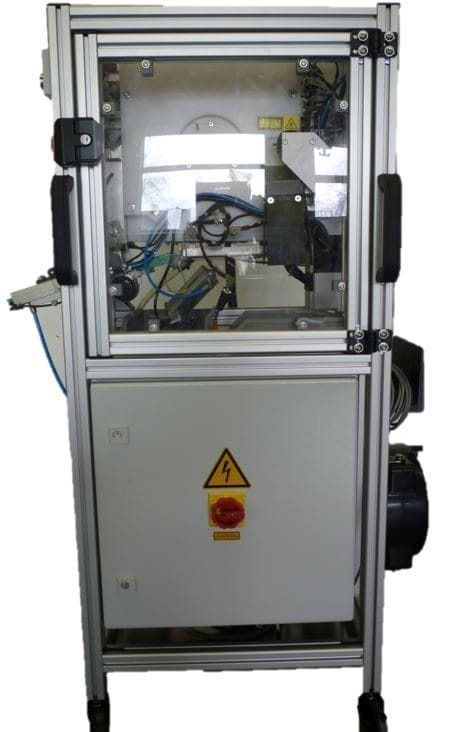 Industriemaschine mit transparentem Gehäuse und Bedienfeld, das die internen Mechanismen und ein Warnschild zeigt.