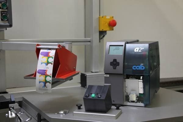 Industriemaschine an einer Fertigungslinie mit Touchscreen-Bedienfeld und rotem Sicherheitsknopf an einer Metallschiene.
