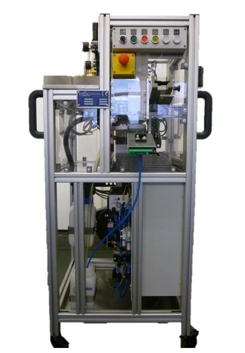 Industriemaschine in einem Metallrahmengehäuse mit sichtbarer Verkabelung, Schläuchen und einem gelben Not-Aus-Knopf.
