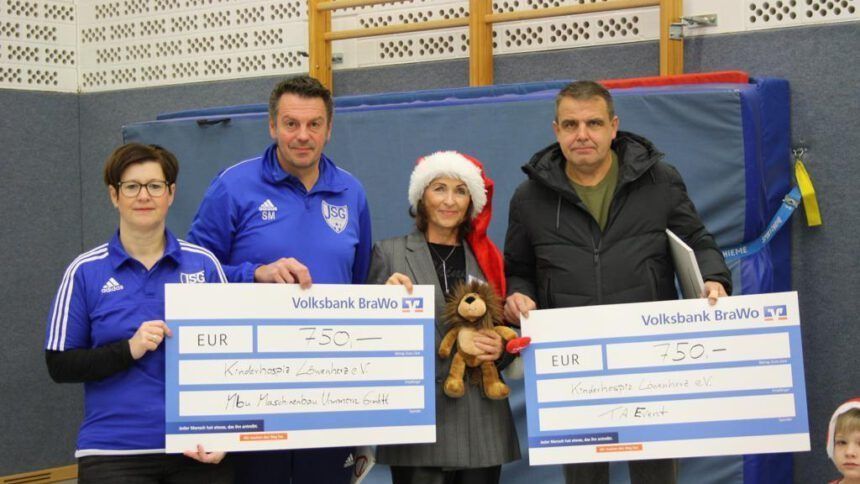 Vier Personen halten bei einer Veranstaltung in einem geschlossenen Raum überdimensionale Schecks und einen Teddybären als Preis vor einer blauen Matte in den Händen.