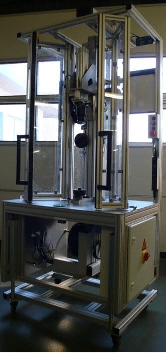 Industrielle Prüfmaschine im Labor, mit Metallrahmen und geschlossenen beweglichen Teilen.