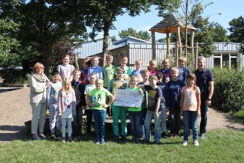 Eine Gruppe von Menschen posiert im Freien mit einer großen Präsentationstafel in einer sonnigen Gartenlandschaft.