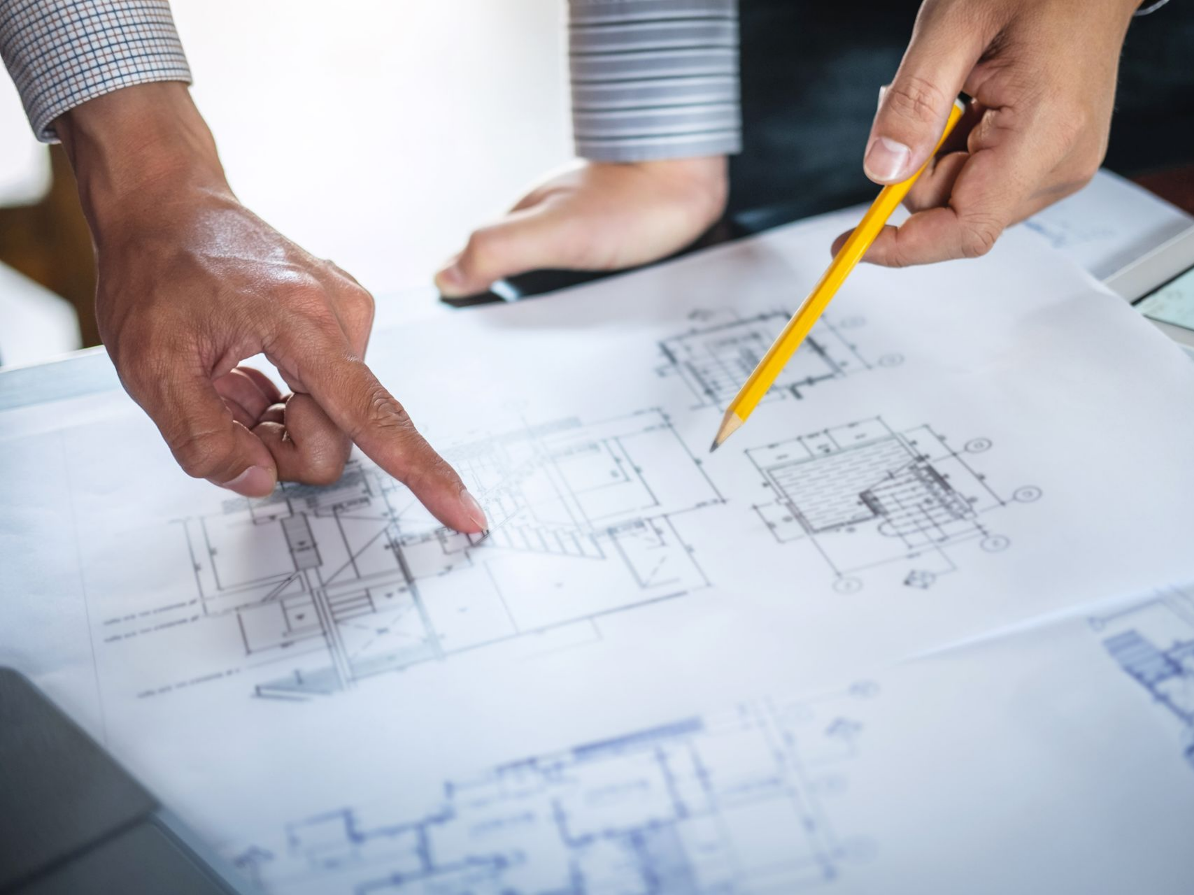 Deux personnes examinent des plans, l'une montre du doigt, l'autre tient un crayon.