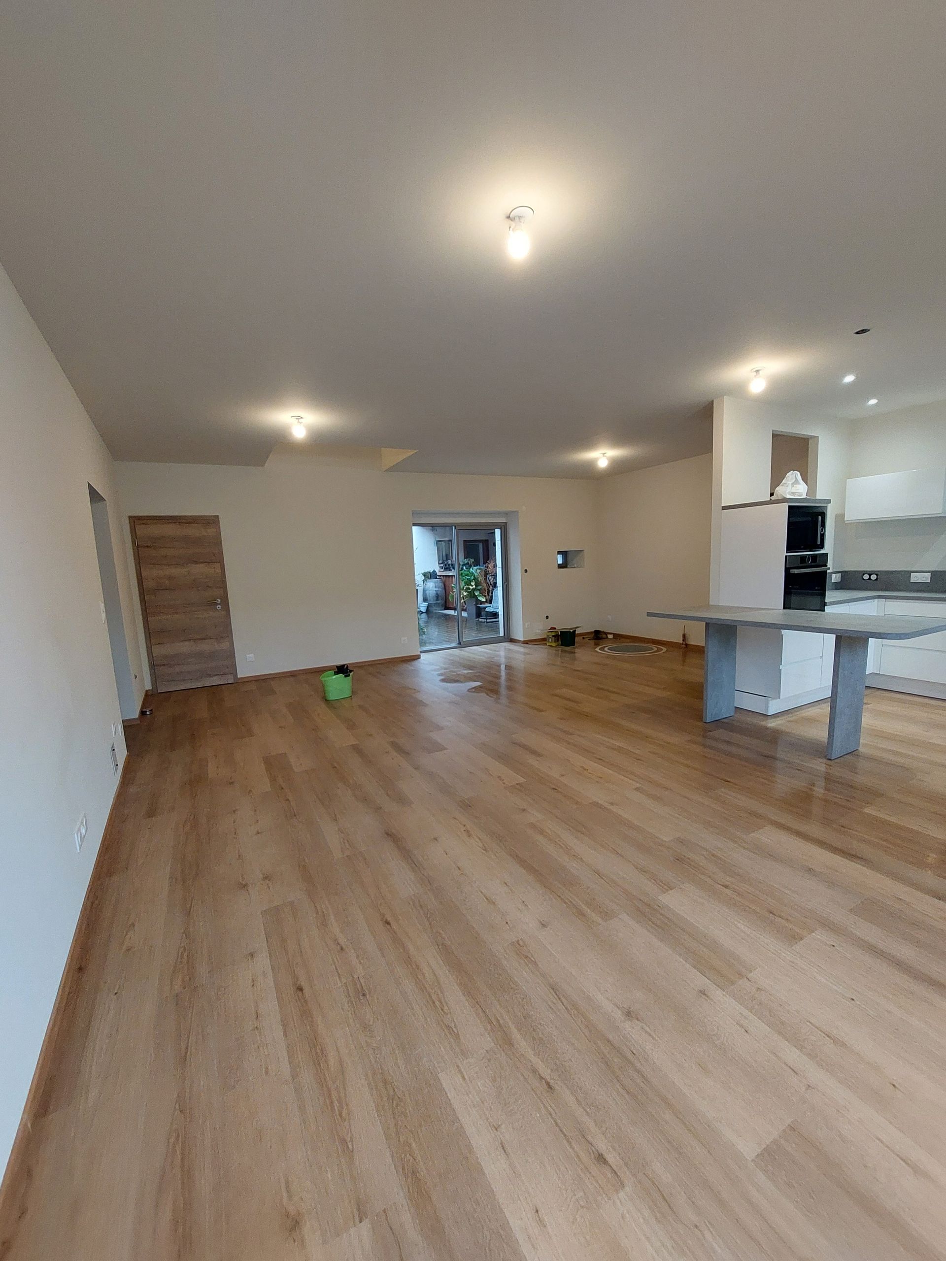 Pièce spacieuse avec parquet, murs blancs et éclairage encastré. Une porte-fenêtre coulissante donne sur l'extérieur.