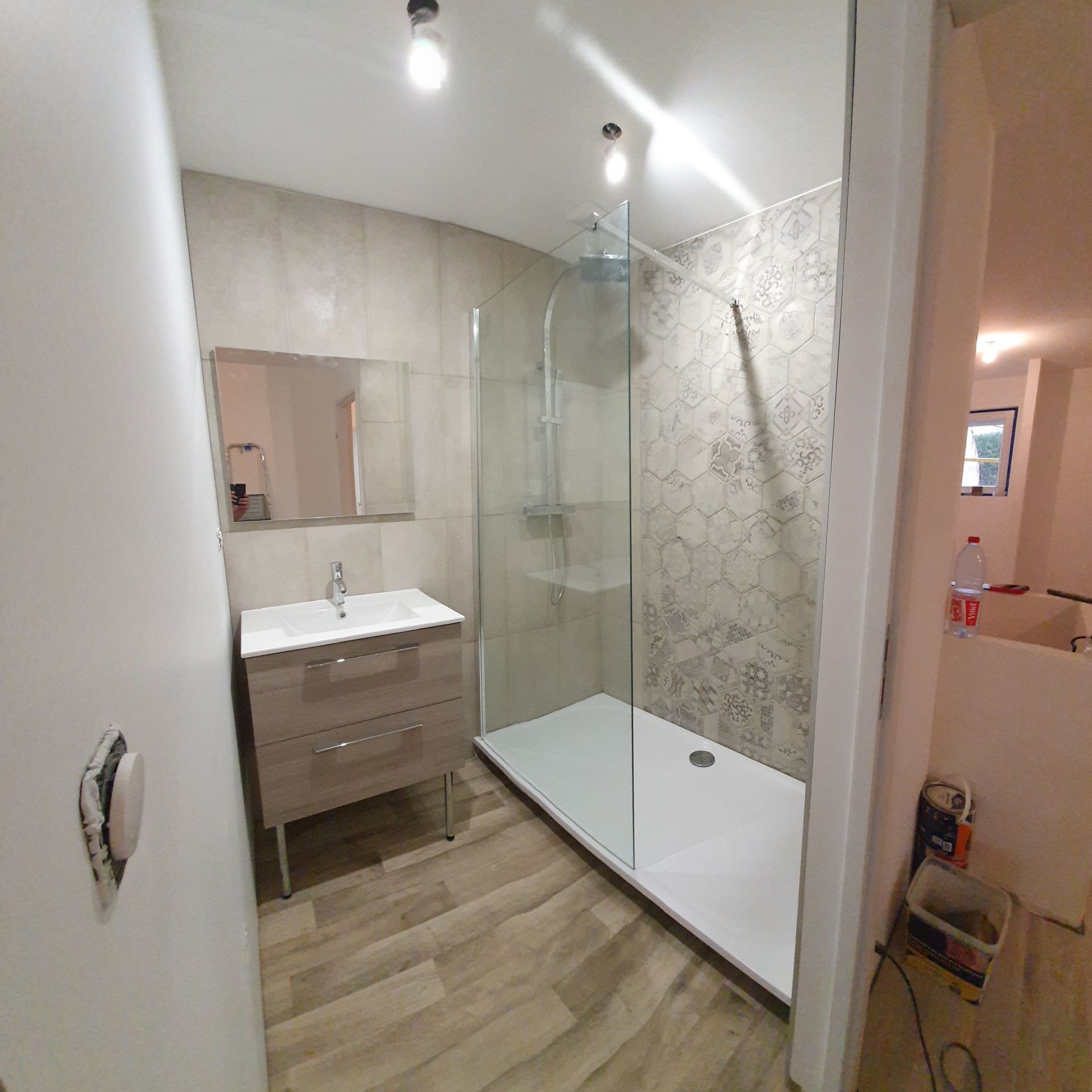 Salle de bains avec douche, meuble pour lavabo et carrelage mural et au sol imitation bois clair.