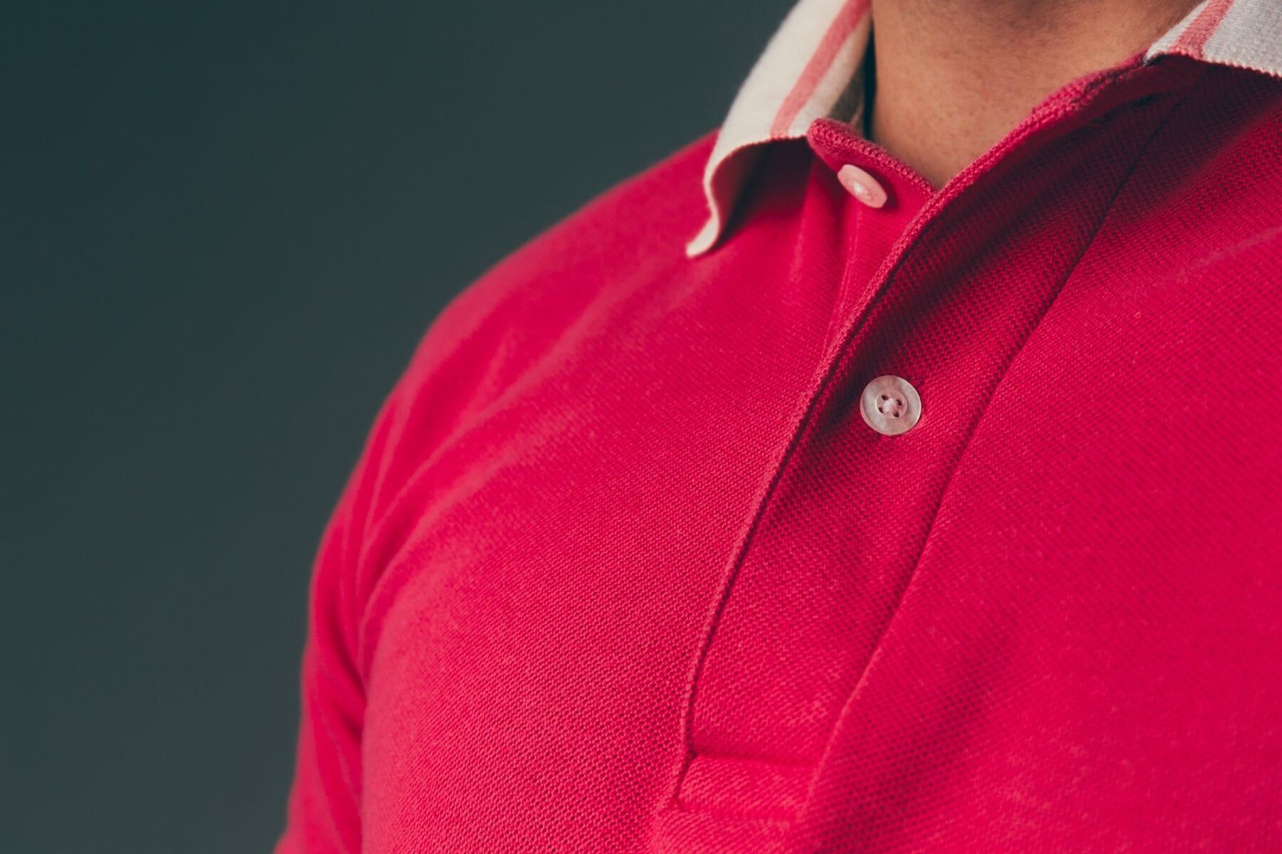 Close-up de uma pessoa vestindo uma camisa de rugby vermelha brilhante com gola branca contra um fundo escuro.