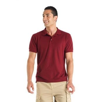 Homem vestindo camisa polo bordô e bermuda cáqui sorri, em pé em frente a um fundo branco.