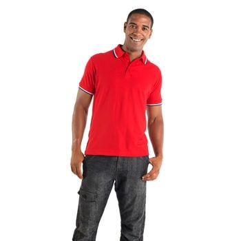 Homem sorridente, vestindo uma camisa polo vermelha com detalhes brancos e calça jeans escura, com as mãos nos bolsos.