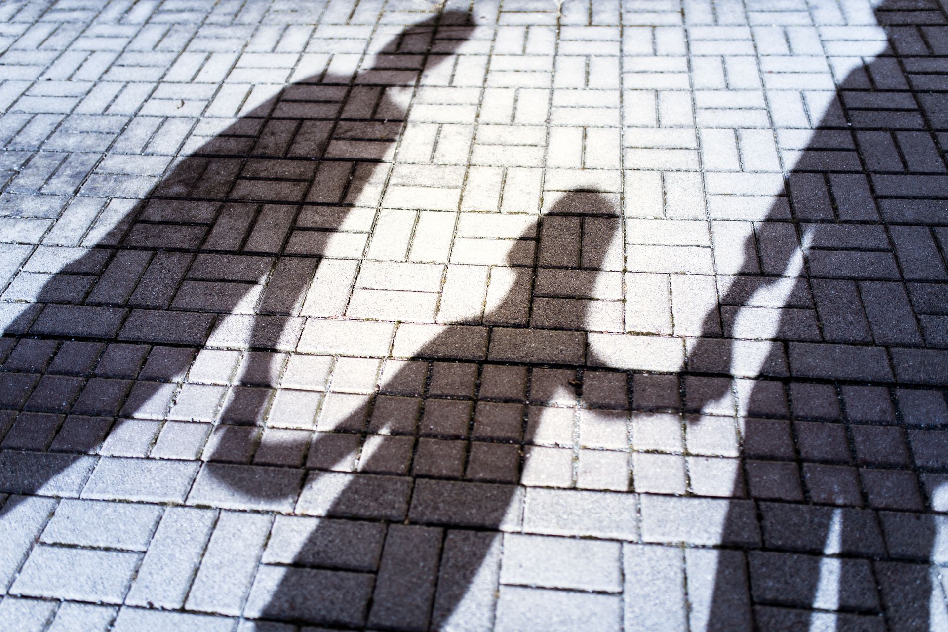 Ombres de trois personnes sur un pavé ensoleillé, l'une d'elles levant le bras.