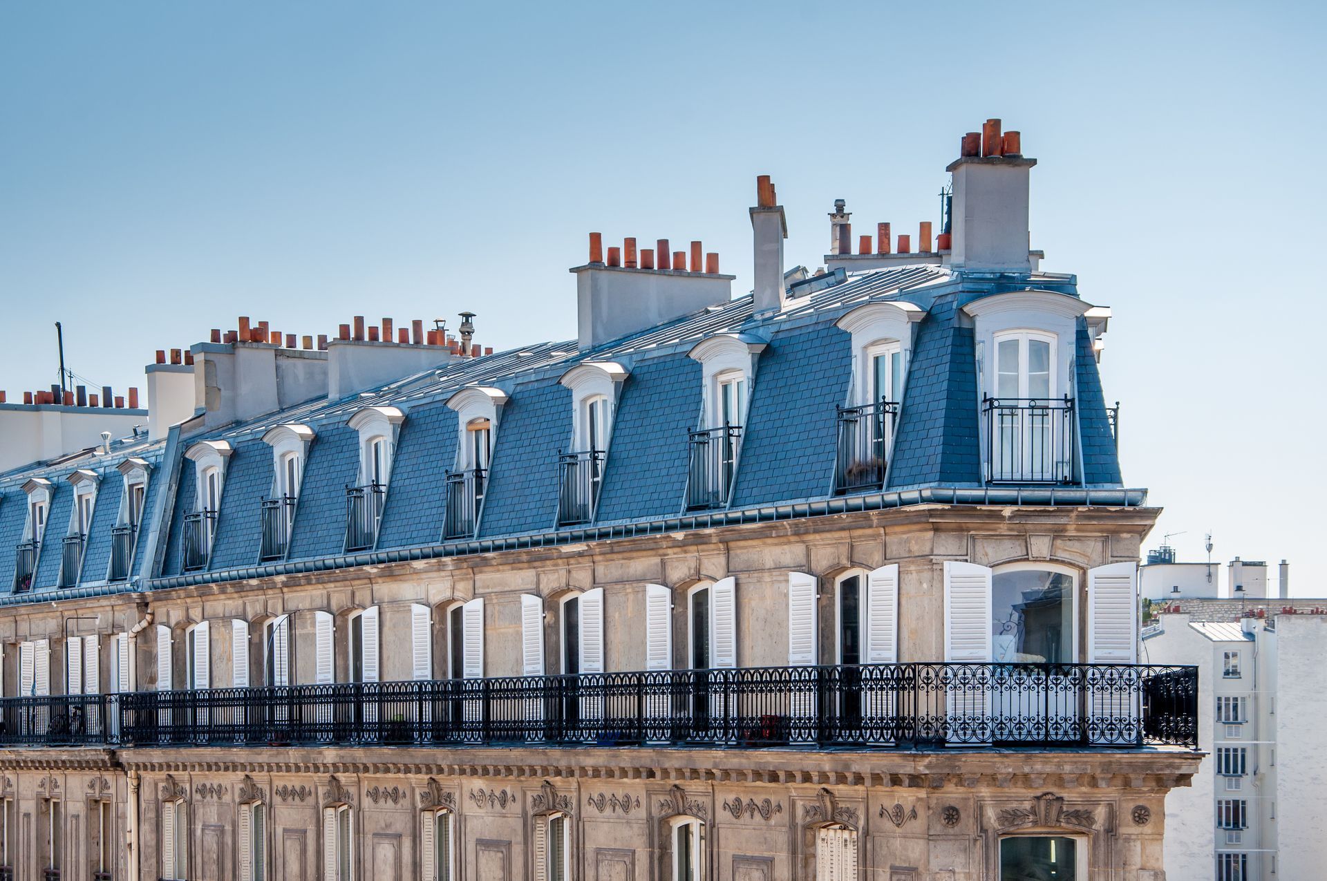 Toit parisien avec toit mansardé en ardoise bleue, cheminées et balcons ornés sous un ciel dégagé