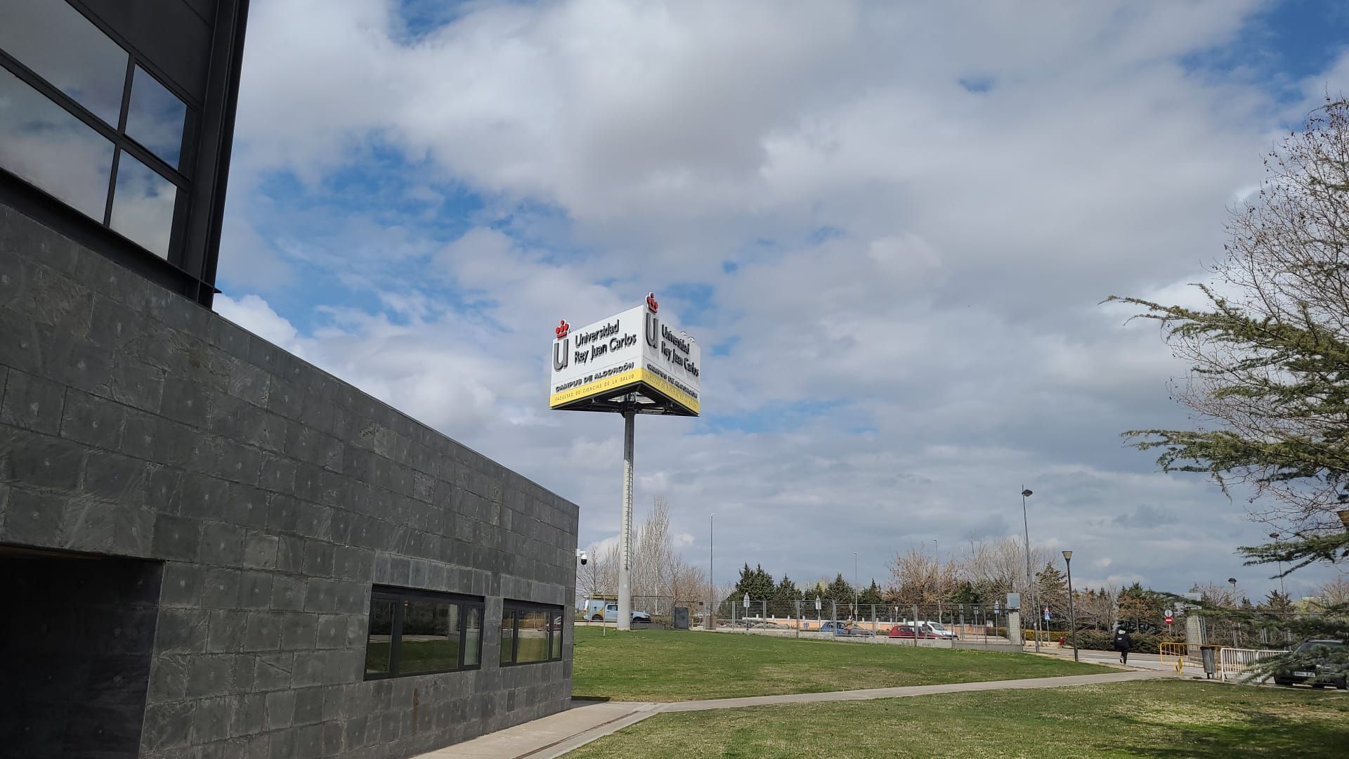 Cartel publicitario en un parque con un edificio moderno en primer plano; cielo nublado.