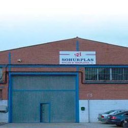 Edificio de ladrillo con puerta azul y cartel de Sohurplas, coches aparcados delante.