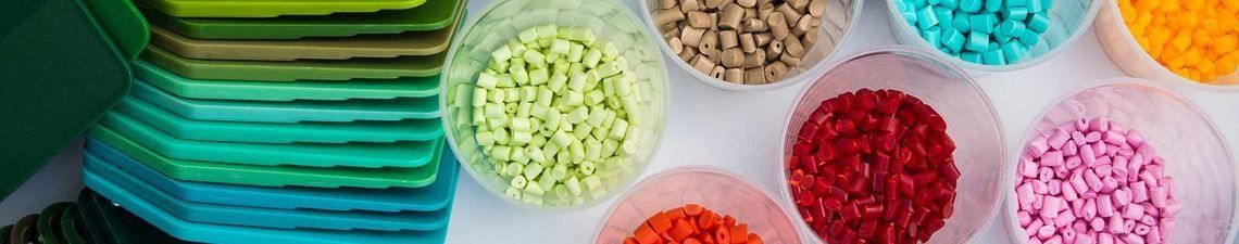 Bolitas de plástico de colores en varios tonos, expuestas en pequeños recipientes transparentes sobre un fondo blanco.