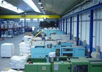 Interior de almacén con máquinas de moldeo por inyección de plástico; pilas de materiales, grúa aérea.