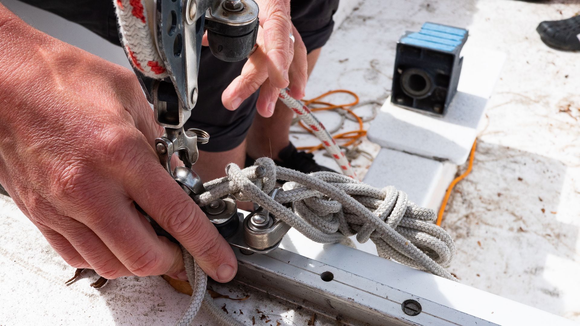Une personne ajuste les cordages sur le pont d'un voilier, en fixant une corde à un taquet et un système de rail métalliques.