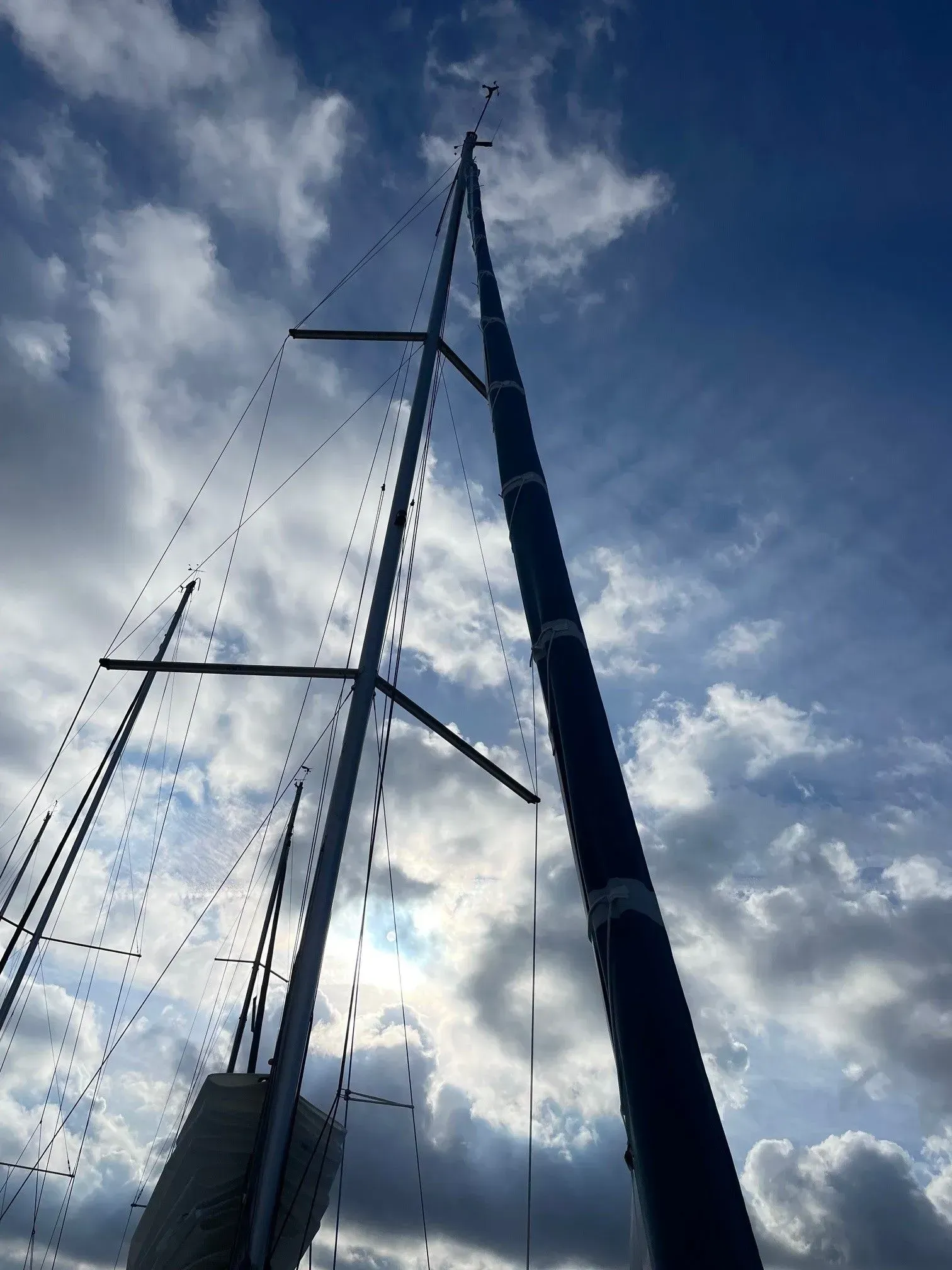 Vue en contre-plongée de deux mâts de voiliers s'élevant vers un ciel bleu nuageux.