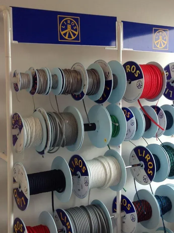 Un présentoir de vente au détail avec de nombreuses bobines de cordes et de cordons de couleurs variées, portant le logo Liros.