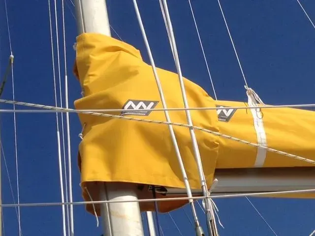Une bâche jaune vif enveloppe le mât et la bôme d'un voilier sur fond de ciel bleu clair.