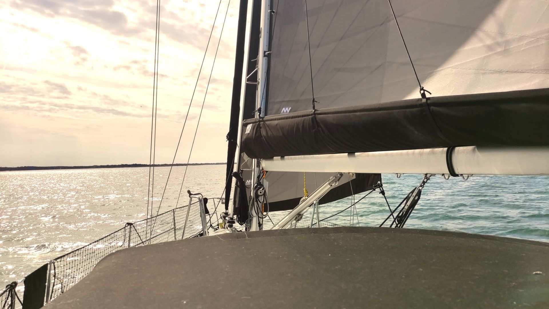 Une personne vêtue d'une veste bleue dirige un petit voilier à la coque vert menthe et au pont en bois sur une eau bleue agitée.