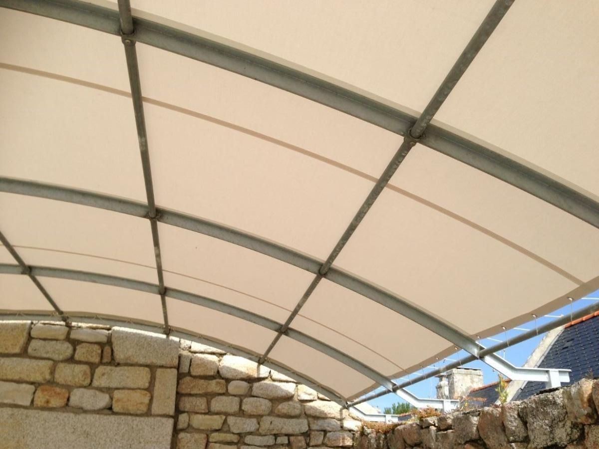 Un auvent blanc incurvé, soutenu par une structure métallique, est installé au-dessus de murs en pierre à l'extérieur.