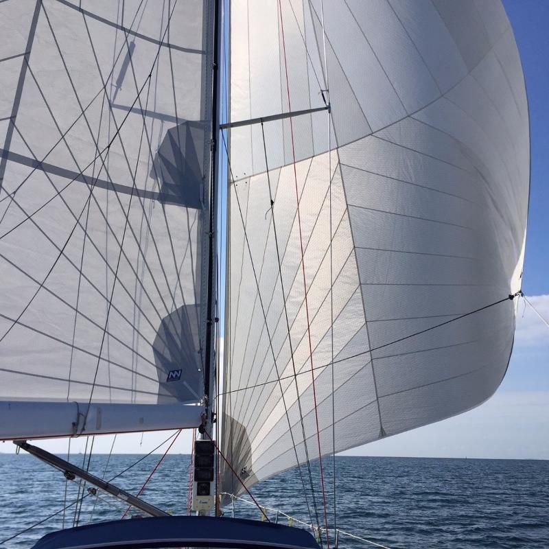 Voiles blanches d'un voilier gonflées par le vent sur un ciel bleu clair au-dessus de l'océan.