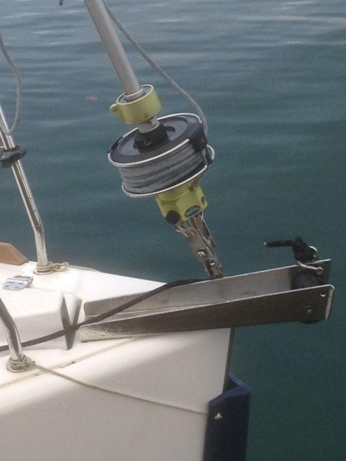 L'étrave d'un voilier, équipée d'un davier d'ancre en acier inoxydable et d'un enrouleur monté sur le pont au-dessus d'eaux calmes.