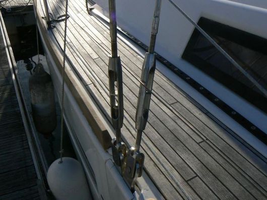 Vue en plongée des accessoires de pont d'un voilier, montrant deux tendeurs métalliques fixés à des supports de pont à côté du platelage en bois.