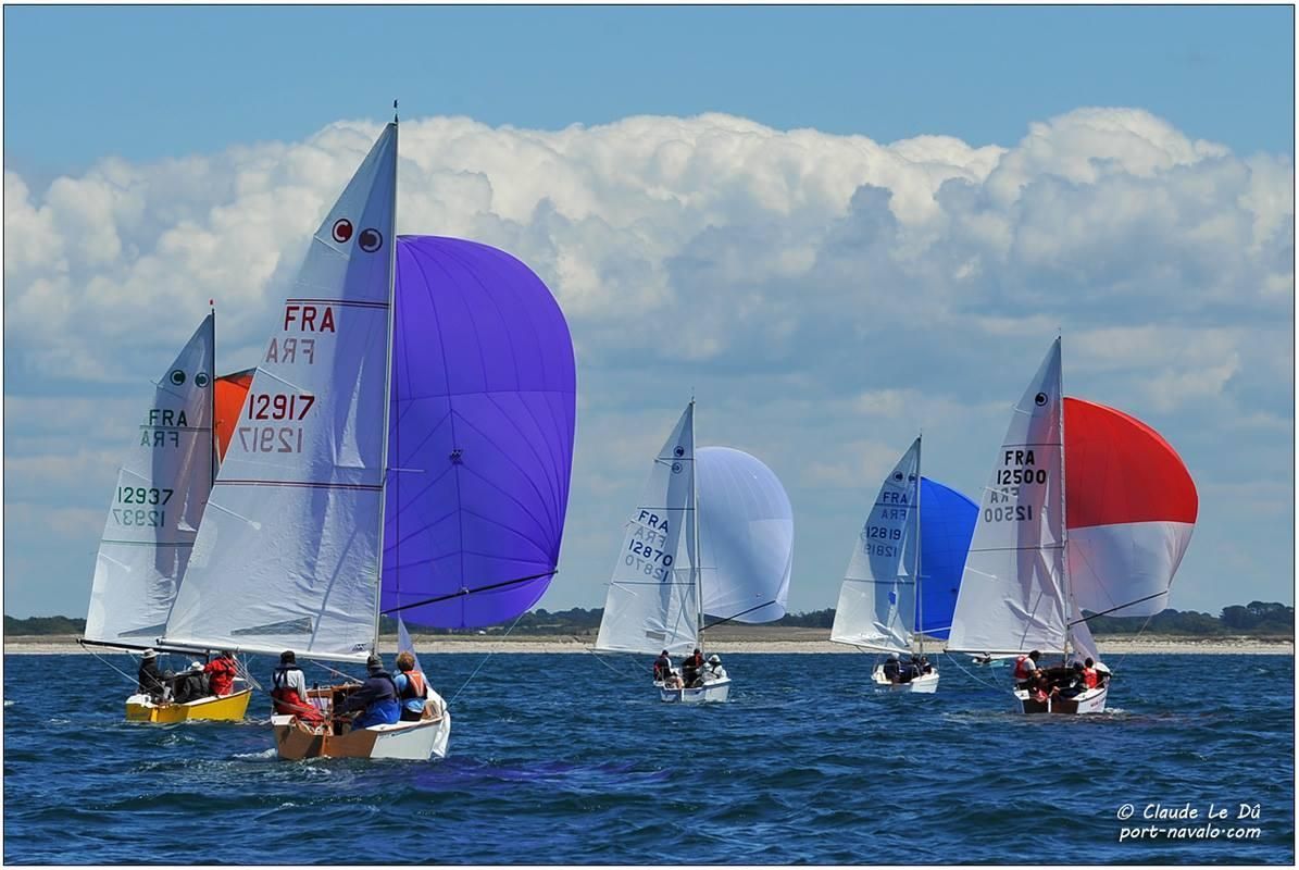 Un groupe de voiliers aux spinnakers colorés fendant l'océan sous un ciel nuageux.