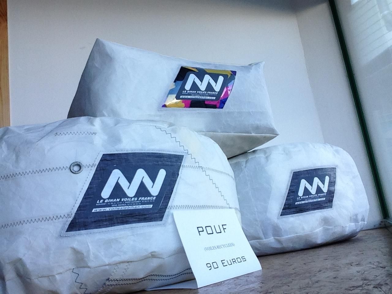 Trois poufs clairs, de style toile à voile, avec des logos NN, dont un avec une petite étiquette portant la mention POUF à l'avant.