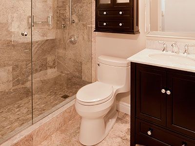 Baño con paredes de mármol, ducha de cristal, inodoro blanco, tocador oscuro y mueble.