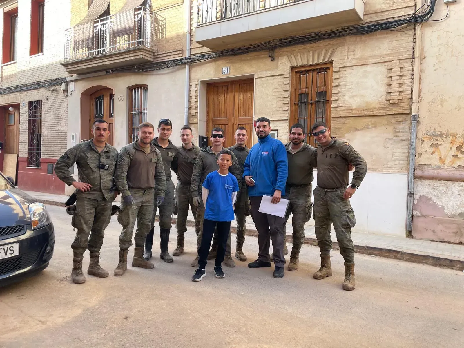Un grupo de soldados y dos civiles posan en la calle. Un niño está de pie en el medio, sonriendo.