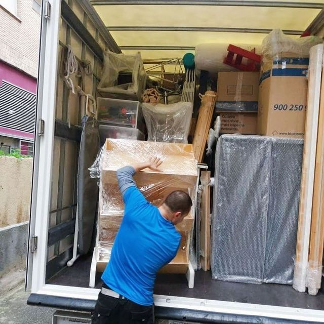 Un hombre carga muebles en un camión de mudanzas. El hombre de la camisa azul está envolviendo un armario con plástico 