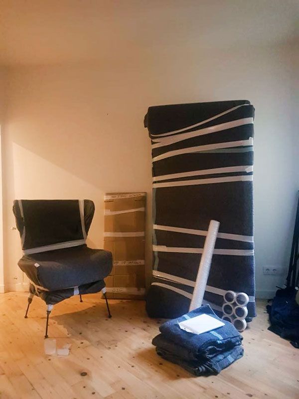Una habitación con muebles envueltos para su mudanza: una silla, dos objetos altos y artículos atados 