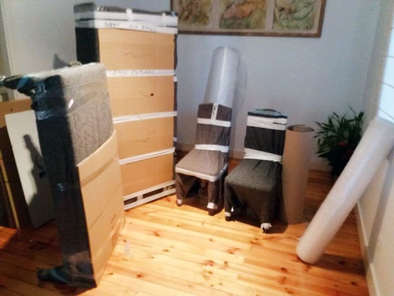 Cajas y muebles envueltos en plástico, listos para la mudanza, reposan sobre el suelo de madera.