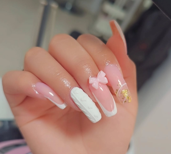 Mano con uñas francesas largas y rosadas, adornada con una uña texturizada blanca, un lazo rosa y un detalle de papel dorado.