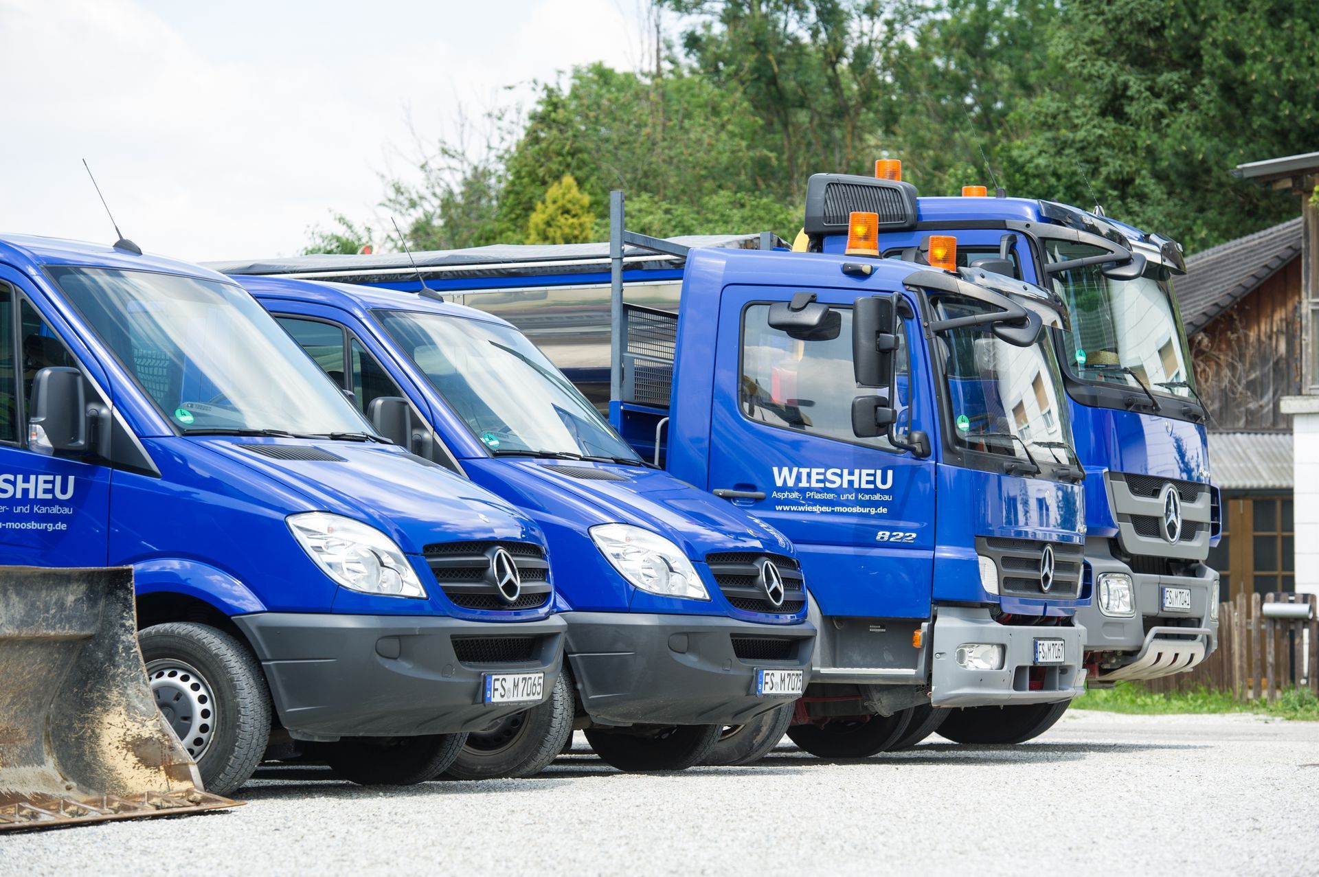 Ein Bauarbeiter benutzt ein Vermessungsinstrument auf einer Baustelle. Weitere Arbeiter in Warnwesten und Schutzhelmen sind zu sehen.