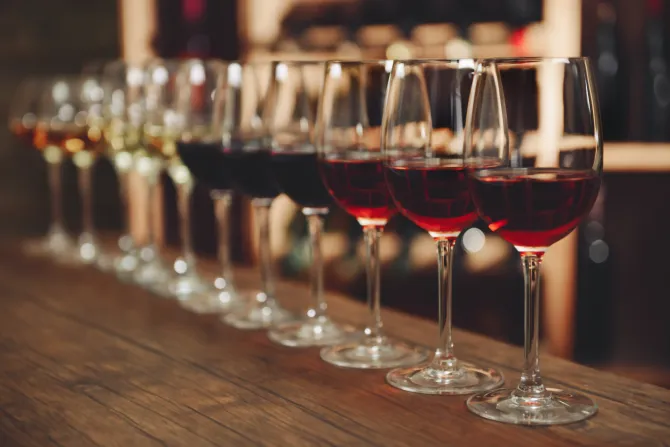 Copas de vino alineadas sobre una superficie de madera, de diferentes tonos de rojo, blanco y ámbar.