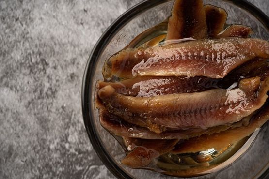 Cuenco de filetes de arenque en escabeche sobre una superficie gris.