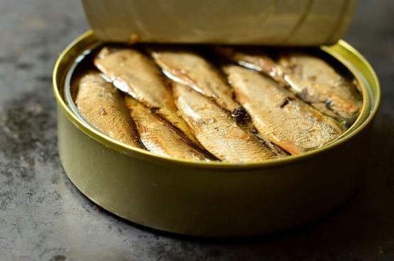 Lata abierta de sardinas en aceite, pescado de color marrón dorado, lata verde claro, superficie gris oscuro.